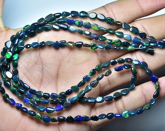 Pode incluir: Um fio de contas de opala verde escuro e preto, com reflexos iridescentes de cor. As contas são em forma de lágrima e enfiadas em um fio fino.