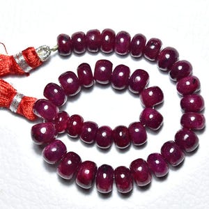 Puede incluir: Un collar de cuentas de rubí rojo oscuro pulidas. Las cuentas en forma de barril están ensartadas en espiral. Borlas rojas con detalles plateados están unidas a los extremos. Las cuentas miden aproximadamente 0,5 cm de diámetro.