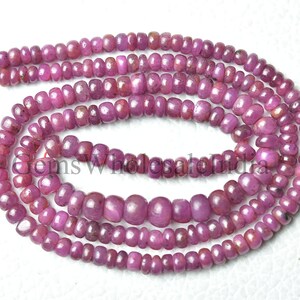 May include: A strand of pink ruby beads, each bead is faceted and has a slightly rounded shape. The beads are strung on a clear thread and are arranged in a loose coil.