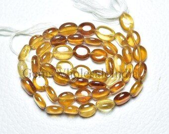 May include: A strand of oval-shaped, translucent, golden yellow gemstone beads. The beads are strung on a white thread with a white tassel at the end.