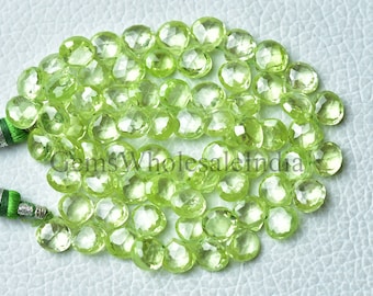 May include: A strand of light green peridot gemstone beads. The beads are faceted and have a round shape. The beads are strung on a string with a green tassel at each end.