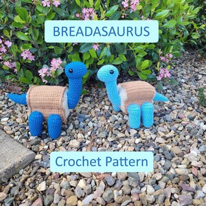 Puede incluir: Dos juguetes de dinosaurio de crochet, uno azul y otro azul claro, están sentados en un lecho de pequeñas piedras. Los dinosaurios llevan conchas de crochet marrones. El texto "BREADASAURUS Crochet Pattern" se muestra sobre un fondo azul.