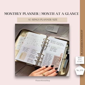 May include: An open A5 ring planner with gold rings, displaying a monthly calendar and to-do lists. The planner is in a zippered case, with a pen and a hand with black nail polish visible. Text on the image reads "MONTHLY PLANNER | MONTH AT A GLANCE".