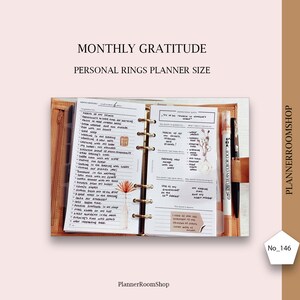 May include: A close-up of a brown leather-bound planner with a white page open to a monthly gratitude log. The page is filled with handwritten notes and a small floral illustration. The planner is open to a page with the heading "Monthly Gratitude" and the text "Personal Rings Planner Size".