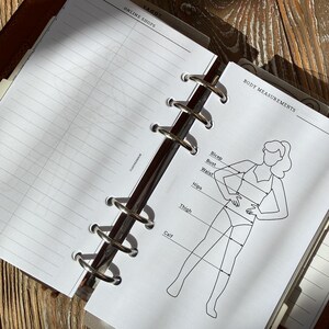 Könnte beinhalten: Eine Ringbucheinlage mit einer weißen Seite, die eine schwarze Strichzeichnung einer menschlichen Figur zeigt. Das Diagramm enthält Beschriftungen für Körpermaße: Bicep, Bust, Waist, Hips, Thigh und Calf. Die gegenüberliegende Seite ist liniert.