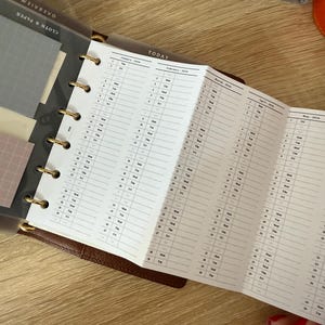 May include: A brown leather ring-bound planner featuring a fold-out white paper insert with a 2024 calendar. The insert displays months from January to May in vertical columns with dates and days of the week. A translucent divider labeled TODAY is visible.