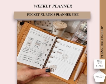 Puede incluir: Una agenda semanal encuadernada en cuero marrón con anillas doradas. La agenda está abierta a una semana con un diseño de cuadrícula. La agenda está etiquetada como "Weekly Planner" y "Pocket XL Rings Planner Size".