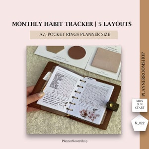 May include: A brown leather A7 pocket rings planner open to a monthly habit tracker. The planner includes gold rings, a floral design, and the text "MONTHLY HABIT TRACKER | 5 LAYOUTS". Additional stationery is visible.