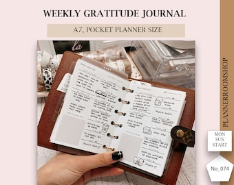 May include: A weekly gratitude journal in A7 pocket planner size. The journal has a brown leather cover and is open to two pages with handwritten text and illustrations. The text includes phrases like "I'm grateful for" and "Happy walls".