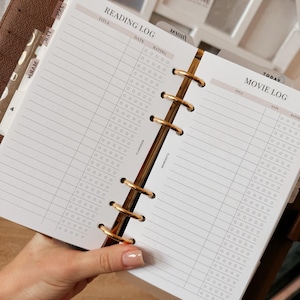 May include: A planner open to Reading Log and Movie Log pages. The pages are lined with spaces for title, date, and rating. The planner has gold-coloured rings and a brown leather cover. The words "sweet" and "get it done" are visible in the background.
