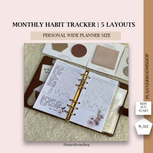 May include: A personal wide planner with a monthly habit tracker. The planner is open, revealing a detailed layout with gold rings and floral accents. The image also shows sticky notes and palette cards.