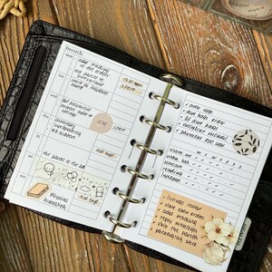 Pode incluir: Agenda aberta com capa de couro preta, exibindo uma programação semanal com anotações manuscritas, adesivos e uma lista de tarefas. O texto "Planning Journaling" é visível.