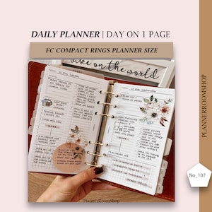 May include: A close-up of an open daily planner with a floral design. The planner is open to the pages for Tuesday, 22nd August and Wednesday, 23rd August. The planner is labelled "FC Compact Rings Planner Size" and "Take on the World".