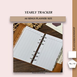 Puede incluir: Una agenda de anillas tamaño A6 con insertos de seguimiento anual en blanco. La agenda abierta muestra un diseño de cuadrícula con columnas para los meses y filas para los días. El texto YEARLY TRACKER y A6 RINGS PLANNER SIZE aparece arriba.