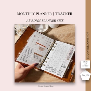 May include: An A5 ring-bound planner with a brown leather cover, featuring a monthly calendar view for May 2023 on the left page and a habit tracker grid on the right page. The pages contain handwritten notes, stickers, and a sticky note.