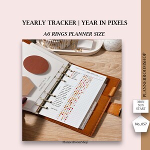 Può includere: Un'agenda ad anelli formato A6 con copertina in pelle color cuoio contenente un inserto Yearly Tracker Year in Pixels. La pagina presenta una griglia con voci dell'umore codificate a colori, incluse le etichette awesome, good, okay, down e depressed.