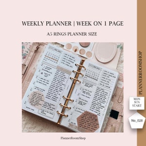 Peut inclure: Un agenda hebdomadaire avec une couverture blanche et des anneaux dorés. L'agenda est ouvert à une page avec des notes manuscrites et des autocollants. L'agenda est intitulé "Weekly Planner | Week on 1 Page" et "A5 Rings Planner Size".