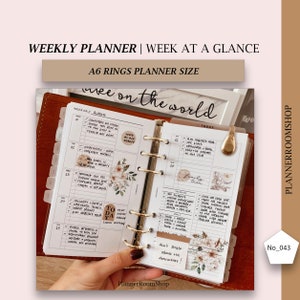 May include: A close-up of an open A6 size planner with gold rings. The planner has a white background with black text and floral stickers. The text on the planner says "Week of August" and "Today".