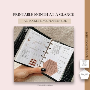 May include: A close-up of a black A7 pocket planner with a monthly calendar and a daily planner page. The planner is open and the pages are filled with handwritten notes and stickers. The planner is labeled "PlannerRoomShop".