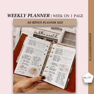 May include: A weekly planner with a white cover and gold rings. The planner is open to a weekly spread with a floral design. The planner is labeled "weekly planner" and "today". The planner is in a brown leather binder. The text "in the world" is visible on a white frame in the background.