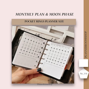 Op de afbeelding: Een zwarte zakagenda met twee open witte pagina's. De pagina's zijn maandelijkse kalenderoverzichten met maanfasen voor januari en februari 2023. De tekst "PlannerRoomShop" staat onderaan de pagina's gedrukt.