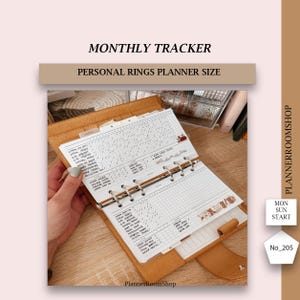 Peut inclure: Un agenda personnel en cuir beige clair avec un insert de suivi mensuel. L'insert a une mise en page en grille avec des lignes et des cases à cocher. L'agenda est ouvert, révélant les pages avec du texte imprimé. Le texte "MONTHLY TRACKER" est en haut.