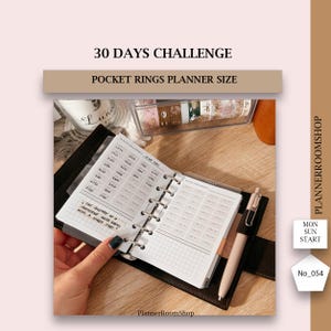 May include: A black leather bound pocket planner with a white 30-day challenge tracker insert. The planner is open to show the tracker and a gridded page. The planner is on a wooden surface with a clear container of washi tape.
