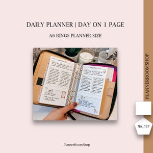 Puede incluir: Una agenda de anillas A6 abierta con cubiertas de cuero beige y cremallera negra. Las hojas de papel blanco presentan un diseño diario con secciones para tareas, notas y un área de cuadrícula. El texto dice DAILY PLANNER | DAY ON 1 PAGE.