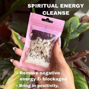 May include: A pink pouch labeled "SPIRITUAL ENERGY CLEANSE" contains a mix of dried herbs and flowers. The text below the label reads: "Remove negative energy & blockages" and "Bring in positivity, abundance & breakthroughs."