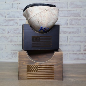 May include: A wooden hat rack with two tiers. The top tier is black and has an American flag design. The bottom tier is brown and also has an American flag design. A baseball cap with a floral pattern is displayed on the top tier.