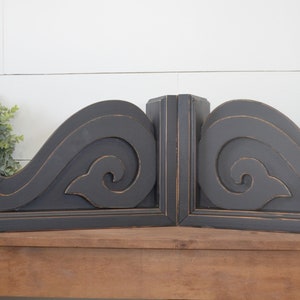 May include: A pair of black wooden corbels with a decorative scroll design. The corbels are distressed and have a rustic look.