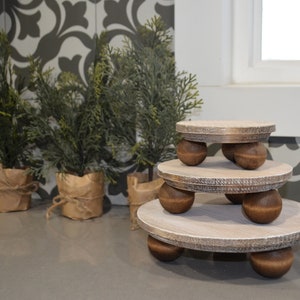 May include: A set of three tiered wooden display stands with a whitewashed finish. Each stand has a round top and is supported by four wooden ball legs.