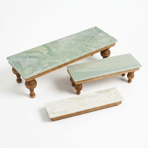 May include: Three rectangular display risers with smooth, polished stone tops in shades of light green and white, each supported by dark brown wooden bases featuring turned, pedestal-style legs for elevation and stability.
