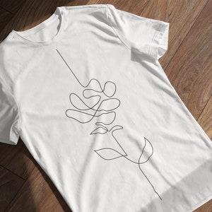 May include: White t-shirt featuring a single-line drawing of a flower on the front.