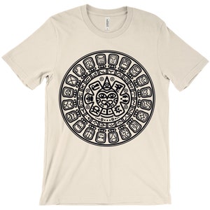 May include: A beige t-shirt with a black and white graphic print of the Aztec calendar. The calendar is a circular design with a central sun god figure and glyphs around the outside.
