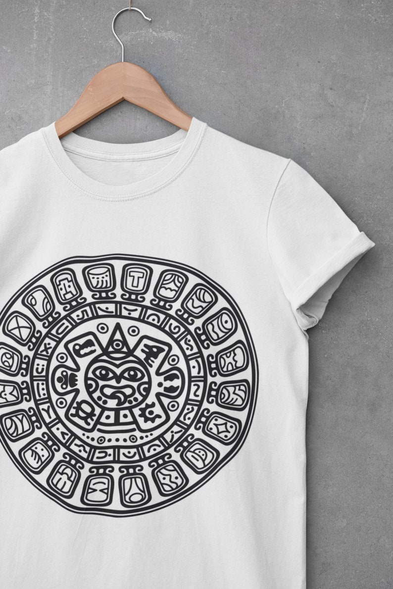 May include: White t-shirt with a black and white graphic print of a circular design with a sun face in the center. The design is reminiscent of an Aztec calendar.