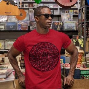 May include: A red t-shirt with a black and white graphic of the Aztec calendar. The calendar is a circular design with glyphs and symbols.