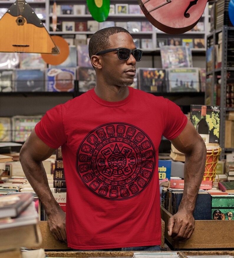 May include: A red t-shirt with a black and white graphic of the Aztec calendar. The calendar is a circular design with glyphs and symbols.