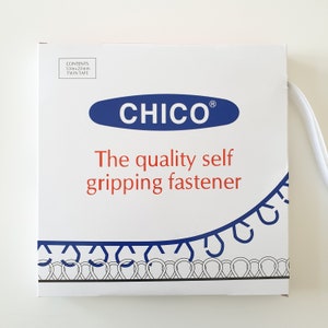 Op de afbeelding: Een witte doos met blauwe en rode tekst. De doos bevat 10 mm x 20 mm dubbelzijdig tape. De tekst op de doos luidt "CHICO® The quality self gripping fastener".