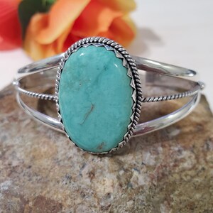 May include: A silver cuff bracelet with a turquoise stone set in a rope design. The stone is a light blue-green color and has a smooth, polished finish.