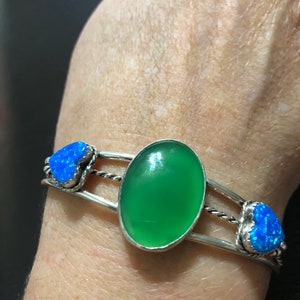 May include: A silver bracelet with a green oval stone and two blue heart-shaped stones.