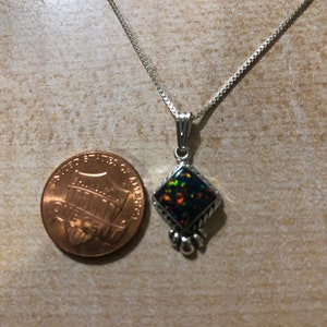 May include: A silver chain necklace with a pendant featuring a black opal gemstone set in a silver diamond-shaped frame with silver accents.