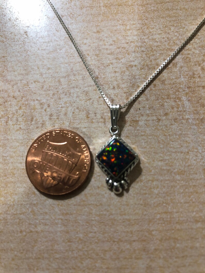 May include: A silver chain necklace with a pendant featuring a black opal gemstone set in a silver diamond-shaped frame with silver accents.