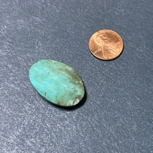 Puede incluir: Una piedra preciosa turquesa en cabuj&oacute;n de forma ovalada, de color azul verdoso con una matriz marr&oacute;n. La piedra es aproximadamente del tama&ntilde;o de una moneda de un c&eacute;ntimo de euro.