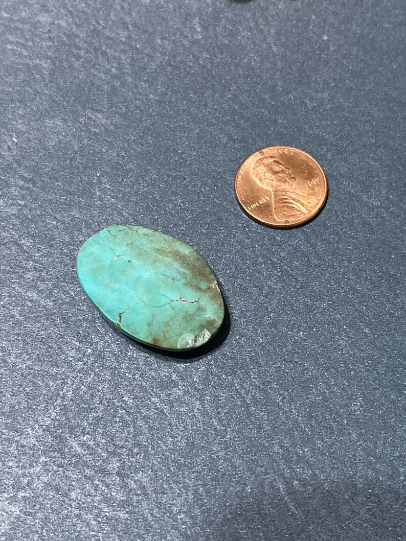 Puede incluir: Una piedra preciosa turquesa en cabuj&oacute;n de forma ovalada, de color azul verdoso con una matriz marr&oacute;n. La piedra es aproximadamente del tama&ntilde;o de una moneda de un c&eacute;ntimo de euro.