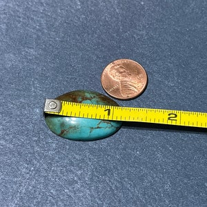 Puede incluir: Una piedra de turquesa en cabuj&oacute;n que mide aproximadamente 2,5 cm de di&aacute;metro. La piedra tiene un patr&oacute;n moteado de marr&oacute;n y verde.