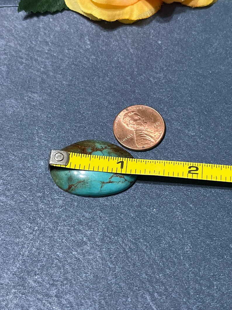 Puede incluir: Una piedra de turquesa en cabuj&oacute;n que mide aproximadamente 2,5 cm de di&aacute;metro. La piedra tiene un patr&oacute;n moteado de marr&oacute;n y verde.