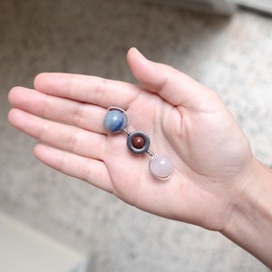 Puede incluir: Un collar de tres cuentas con una piedra azul, roja y rosa. Las cuentas están conectadas por un alambre plateado.