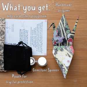May include: A gemstone spinner with a black velvet pouch, an info card with a tutorial link, and a handmade origami crane. The card reads "Gemstone spinner is a creation from Bonsai and Cacti. It connects our love of skill toys & crystals in one. Each stone spins around and it can be used as a knuckleroller to pass around the fingers or as a hand spinner. Can be beneficial for mindfulness, stress relief, finger dexterity, fine motor skill, concentration, meditation and so on. If you like what we make, follow us @bonsaiandcacti Instagram-fb-pinterest. You could tag us with #bonsaiandcacti #crystals".