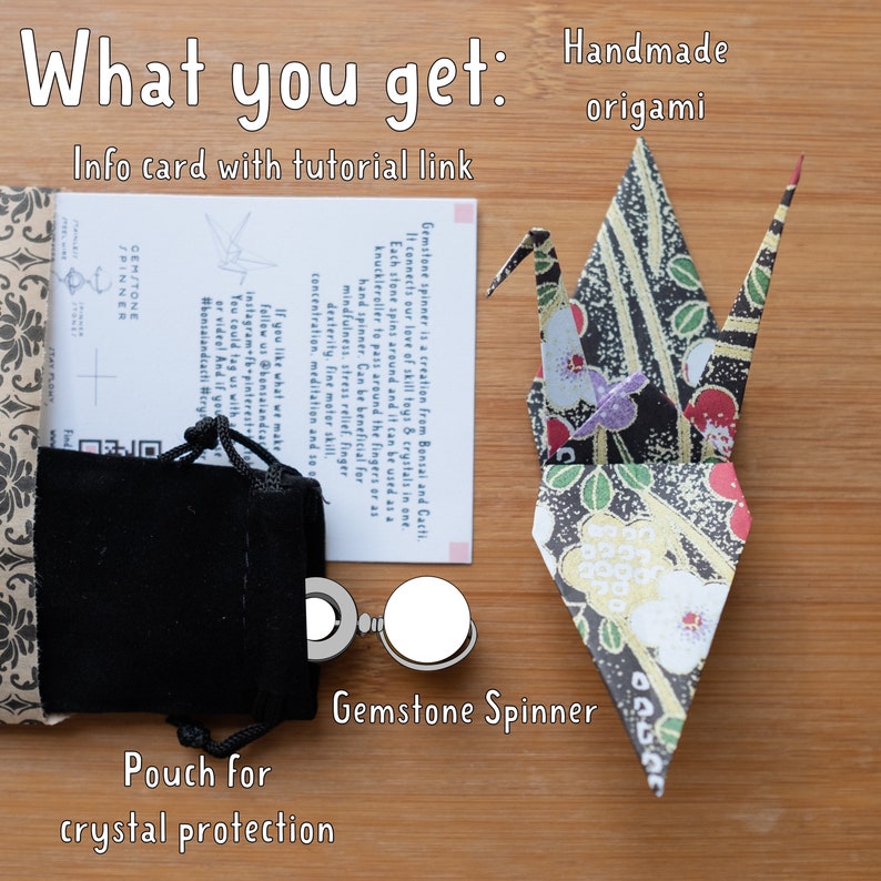 May include: A gemstone spinner with a black velvet pouch, an info card with a tutorial link, and a handmade origami crane. The card reads "Gemstone spinner is a creation from Bonsai and Cacti. It connects our love of skill toys & crystals in one. Each stone spins around and it can be used as a knuckleroller to pass around the fingers or as a hand spinner. Can be beneficial for mindfulness, stress relief, finger dexterity, fine motor skill, concentration, meditation and so on. If you like what we make, follow us @bonsaiandcacti Instagram-fb-pinterest. You could tag us with #bonsaiandcacti #crystals".
